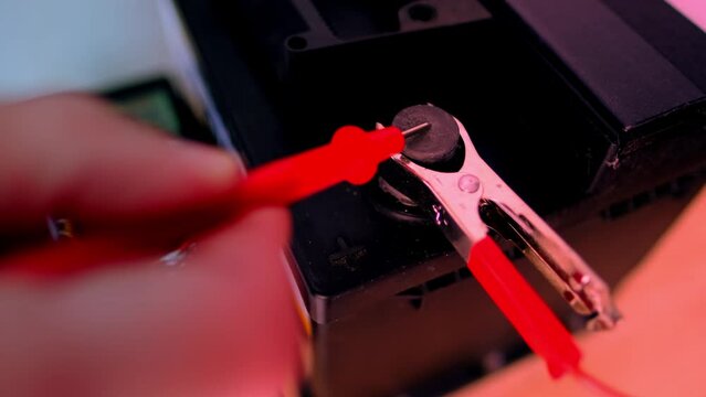 close-up car battery, red terminals are attached to the wires from the charger, the male hand checks the charge level, the concept of checking the battery charge with an electronic multimeter