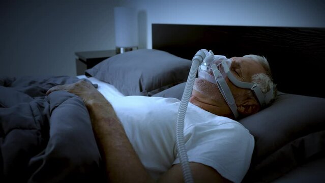 Mature adult sleeping at night while wearing a CPAP mask to treat his Sleep Apnea.
