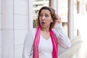 middle age woman looking serious and curious, listening, trying to hear a secret conversation or...