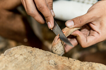 hands of young Latino man carving a figure in wood with knife