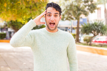 young hispanic man looking happy, astonished and surprised, smiling and realizing amazing and incredible good news