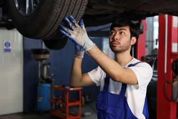 Man technician car mechanic in uniform check or maintenance a lifted car service at repair garage station. Worker holding wrench and fixing vehicle with flashlight. Car center repair service concept