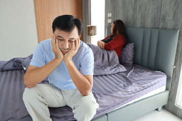 Sad frustrated middle aged asian man sit on bed after having sex while his hands touching head with...