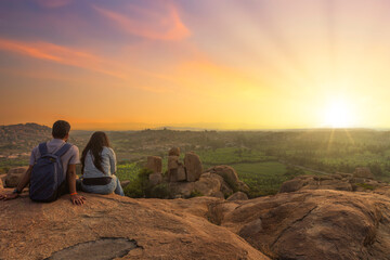 Tourist couple enjoy sunrise from top a hill with scenic landscape view at Hampi Karnataka, India