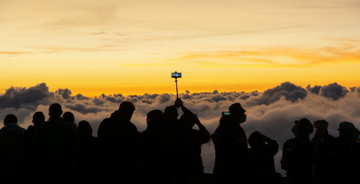 Silhouette person group watching floating sea of clouds,Sea of fog, Sky above clouds,taking cloudscape photos with mobile phones in the morning,sun rising,travel long weekend,Inthanon mountain.