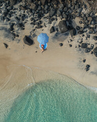 Aerial view of a lady enjoying the beach and the sun under an umbrealla.