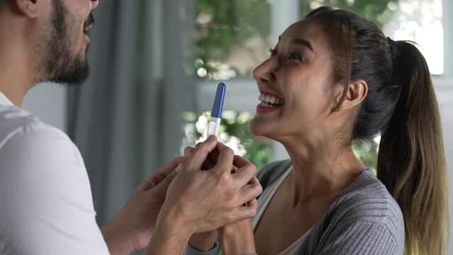 Young Asian couple feeling happy with positive results of a pregnancy test.