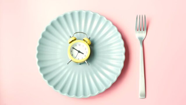 Empty plate with alarm clock and female hand on pink background, intermittent fasting concept.