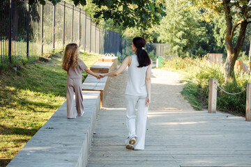 A little daughter holds her mother's hand. Mother and daughter walk in the Park in the summer