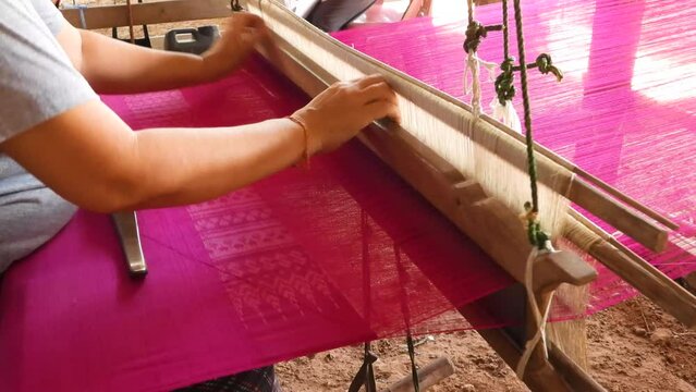 Close up of a woman on a loom to produce Fuchsia Pink Thai silk, by alternating silk threads left and right, Traditional silk production on the Thai countryside.