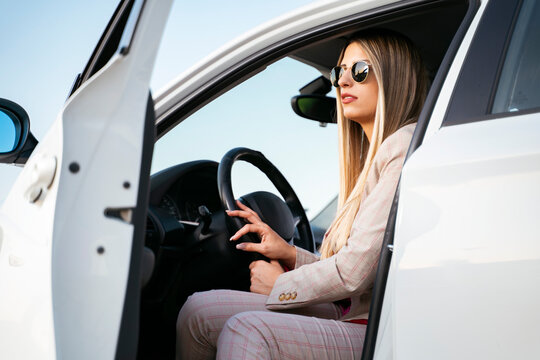 Beautiful young blonde woman exiting her car dressed in suit and pants 