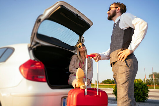 Funny Scene, Woman Sitting In Car Trunk With Legs On Suitcase Man Standing By. High Maintenance Woman 