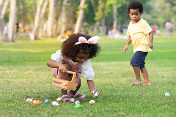 Little African boy and girl wearing bunny ears pick up Easter egg in garden, Easter eggs hunting outdoors