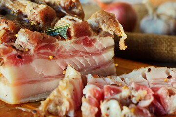 Pieces and slices of salty homemade high-fat meat pork lard cooked with spices on wooden cutting desk close up. Rural salo on table. Traditional food of Ukrainian and Russian cuisine. Selective focus