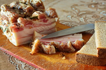 Pieces of salty homemade high-fat meat pork lard cooked with spices, knife and slices of grey bread close up. Rural salo on table. Traditional food of Ukrainian and Russian cuisine 
