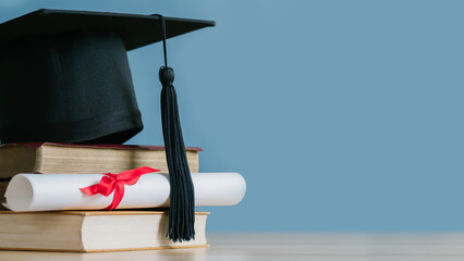 Graduation day.A mortarboard and graduation scroll on stack of books with blue...