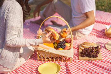 Young couple in love having breakfast together while sitting to picnic on blanket near lake in park