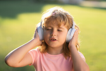 Singing children. Daydreaming child enjoys listens to music in headphones over green grass background. Funny kid in headphones listening to music on summer park or backyard outdoor.