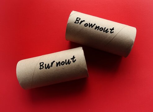 Toilet paper roll on red background with handwritten text BROWNOUT and BURNOUT, concept of brownout syndrome which workers feel overworked, demotivated and disengaged – stage before burnout