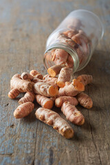 cleaned turmeric rhizomes or roots scattered on table top with a glass bottle, curcuma longa, commonly used spice in cooking and medicine, root-like structure taken in selective focus with copy space