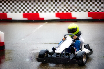 Children's karting competitions, the little racer smoothly passes the turn on the track. Teenage boy driving a go-kart learns to drive a car with a helmet on his head - obrazy, fototapety, plakaty