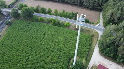 Ansbach, Germany / Bavaria - August 22, 2020: Wide Area Network (WAN) 3G 4G 5G LTE mobile radio broadband transceiver communications tower with, corn field, building , and view from above.