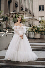Fototapeta premium Full length portrait of beautiful bride in a white gorgeous wedding dress. Fashionable wedding dress with cleavage, wide long sleeves decorated with lace and beads