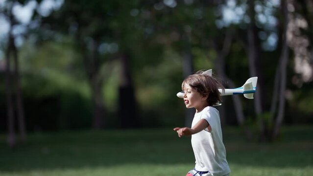 Young boy running with plane toy at park. Carefree Child throwing airplane glider outdoors having fun. Playful kid throws foam plane in sunny beautiful day