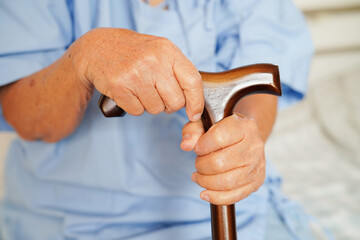 Asian elderly disability woman patient holding walking stick in wrinkled hand at hospital.