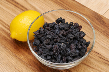 Blue raw raisins in a glass bowl on a wooden table, next to a lemon. 
