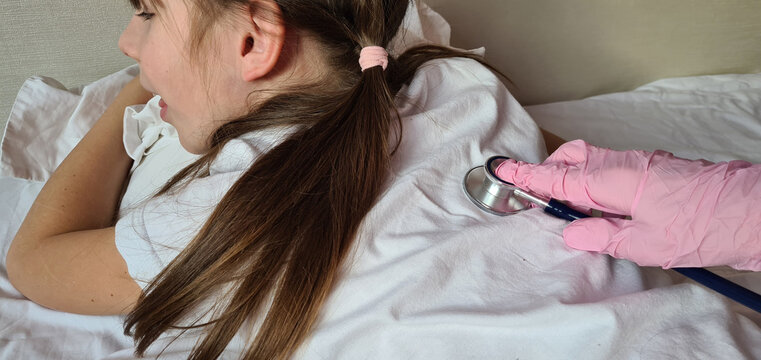 Doctor hand in sterile glove with stethoscope listens to lungs and heart of little girl lying in bed