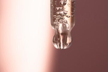 Close-up of a glass pipette with bubbles on an abstract colored background with a spot of light. Beauty procedures, skin care.
