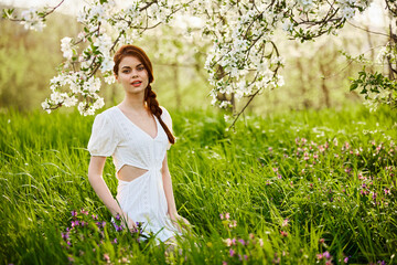 Naklejka na ściany i meble Beautiful woman in a blooming spring garden in a light dress smiling looking at the camera