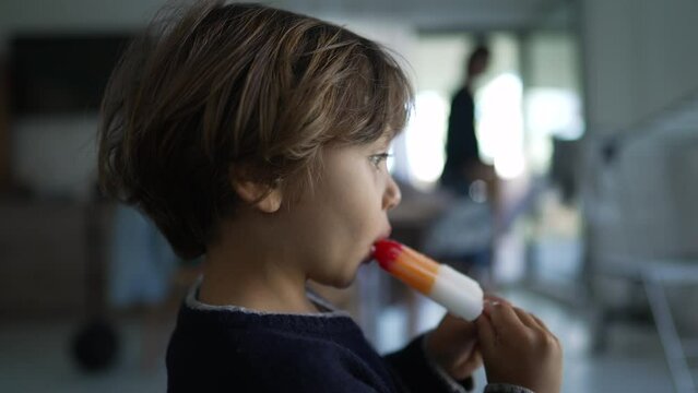 Pensive child eating popsicle ice cream. Profile of small boy holding colorful snack