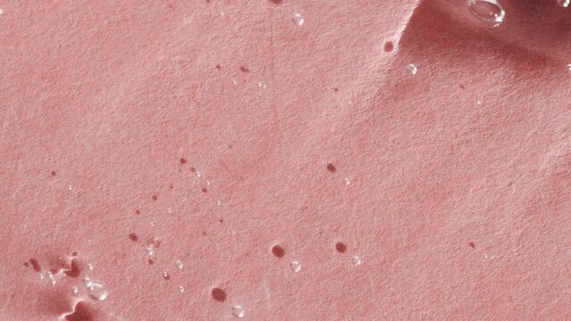 Transparent liquid gel texture close-up, dab of soap, hyaluron flat lay on pink background.