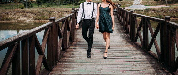 A young and loving couple walk hand in hand along the bridge across the lake. Creative image for your design or illustrations.