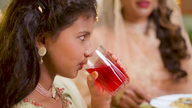 close up shot of Girl kid drinking rose soft drinks during ramadan iftar dinner at home - concept of religious culture, ramzan festive and happiness