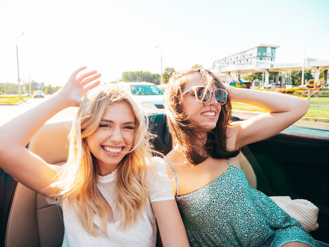 Portrait of two young beautiful and smiling hipster female in convertible car. Sexy carefree women driving. Positive models riding and having fun outdoors. Enjoying summer days. Cheerful and happy