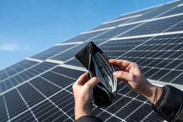Money dollars in a wallet holding hands over a solar panel.