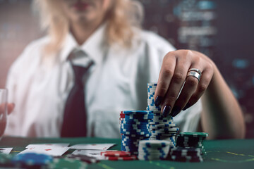 attractive girl holding cards and poker chips at casino table hiding her gaze - obrazy, fototapety, plakaty