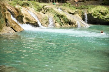 Naklejka premium The idyllic Cambugahay Waterfalls in Siquijor in the Philippines that flow into a natural pool of water surrounded by the light-lit rainforest.