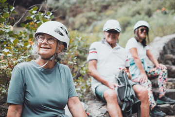 Fototapeta premium Group of smiling people in trekking day in nature, resting in mountain wearing protective helmets. Senior man and women enjoying healthy lifestyle