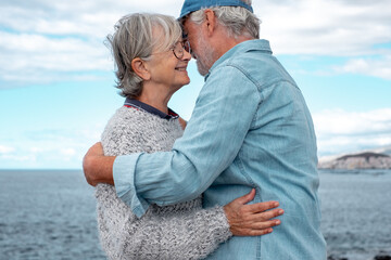 Happy lovely senior couple tenderly embracing by the sea. Smiling elderly man and woman enjoying vacation or retirement outdoor together