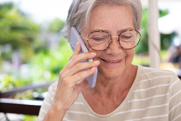 Happy attractive senior woman sitting in outdoor talking at mobile phone, elderly lady smiling using cellphone