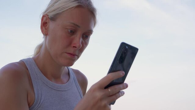 A young blonde woman is typing a message on her phone with a smile on her face. She stays connected to the world through communication and networking during jorney.