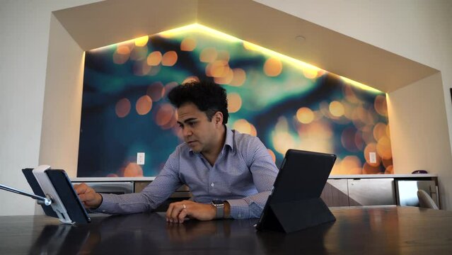 Latin businessman in a modern office. He is working on his tablet, maybe on a video call.
