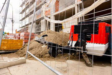 Metal trailer coupling of compressor peeks through wire fence on construction site