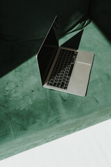 Flatlay laptop computer on green velour sofa with aesthetic sunlight shadows. Minimal work,...
