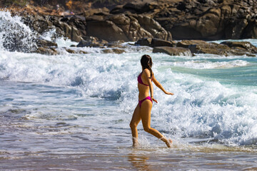 Fototapeta premium A beautiful girl in a pink bikini enjoys a sunny day and plays with the waves on an intimate second bay near Coolum beach, Sunshine coast, Queensland, Australia