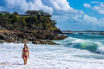Obraz premium A beautiful girl in a pink bikini enjoys a sunny day and plays with the waves on an intimate second bay near Coolum beach, Sunshine coast, Queensland, Australia